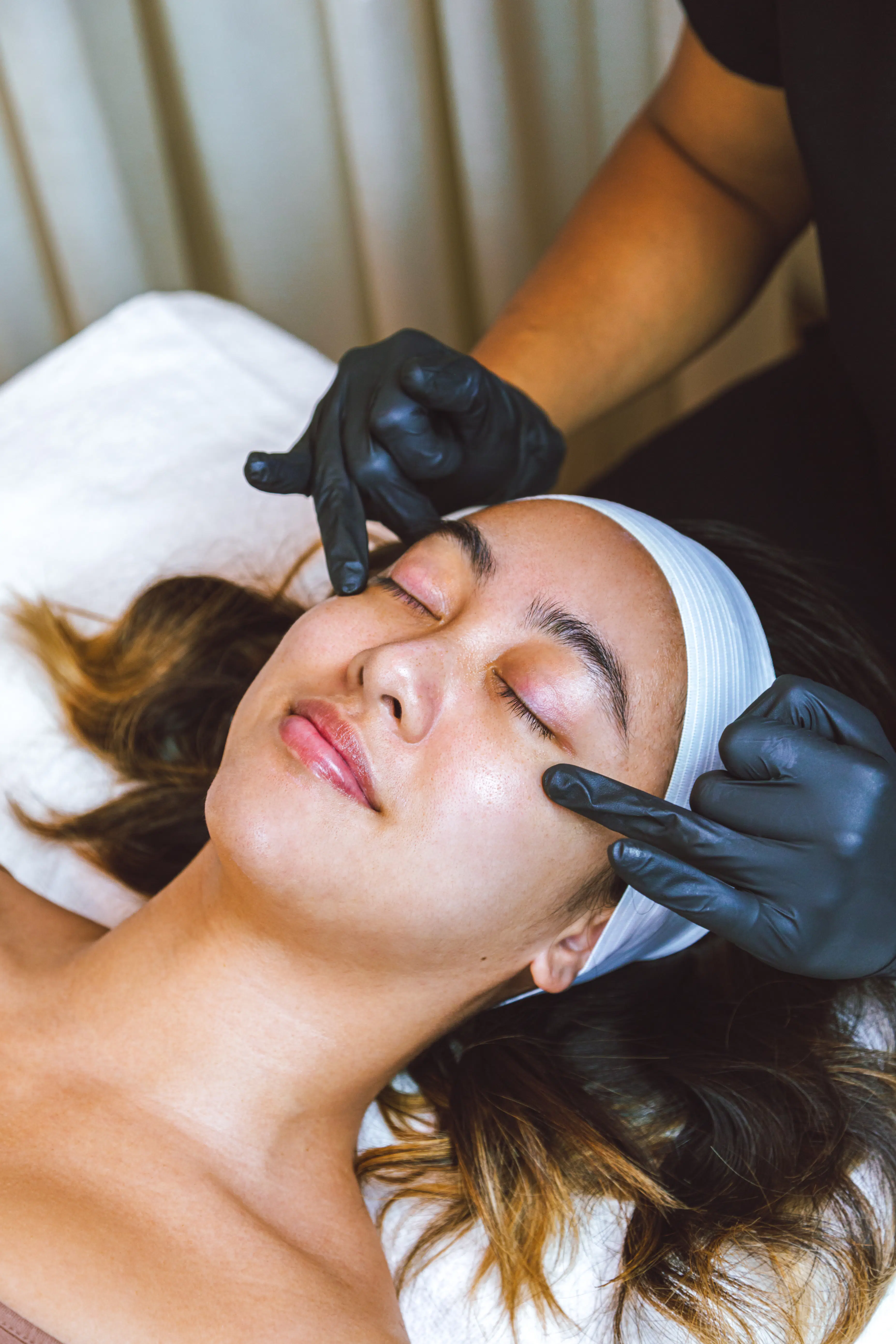 woman in a spa about to get her eyebrows threaded by an esthetician